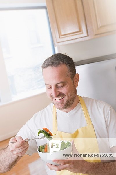 Der reife Mann isst eine Schüssel frischen Salat in der Küche.