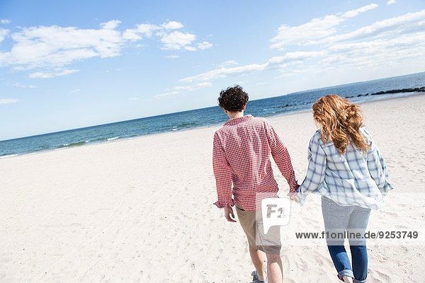 Romantisches Paar  das Hand in Hand am Strand schlendert