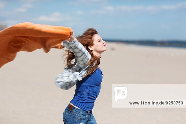 Junge Frau hält Decke am windigen Strand hoch