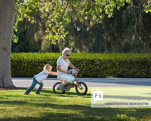Dreijähriger Junge schiebt Großmutter auf Fahrrad im Park