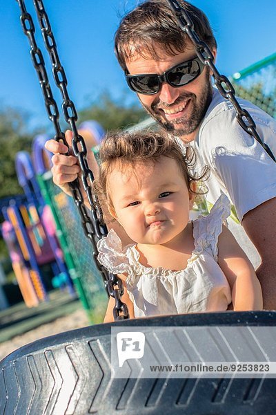 Vater und Kleinkind Tochter ziehen ein Gesicht auf Parkschaukel
