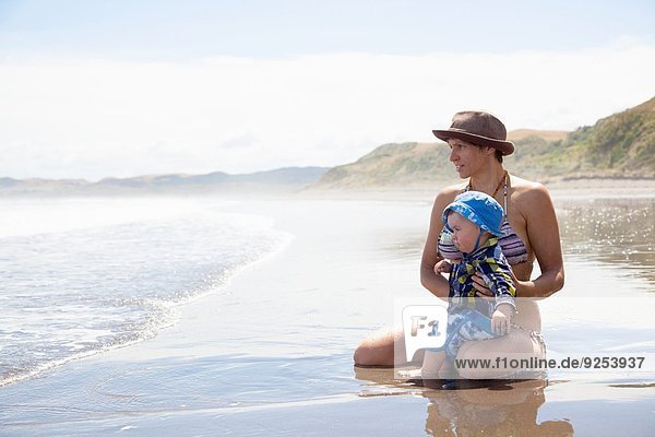 Young woman sitting on beach with baby son