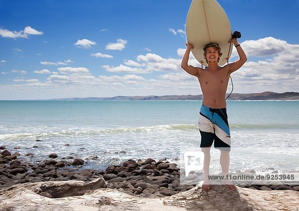 Portrait eines jungen erwachsenen Surfer  der das Surfbrett hochhält.