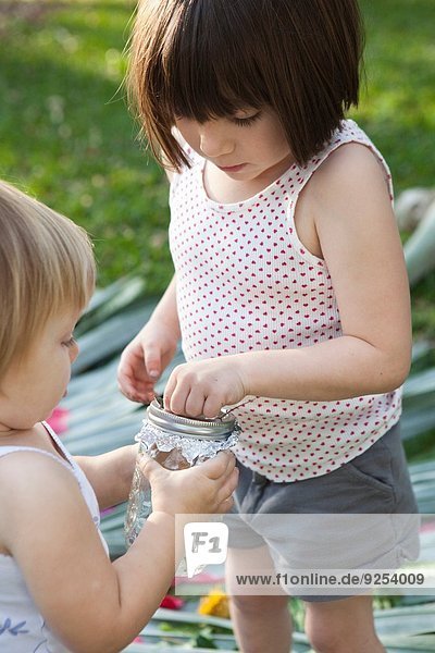 Mädchen und Kleinkind Schwester halten Glas mit grüner Eidechse im Garten