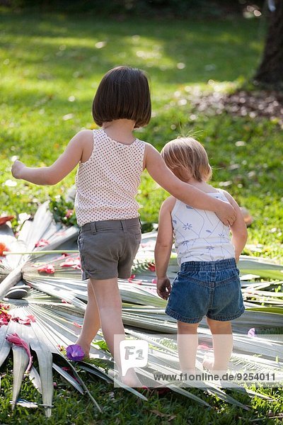Mädchen mit Arm um Kleinkind Schwester mit Blumen- und Blattdisplay im Garten