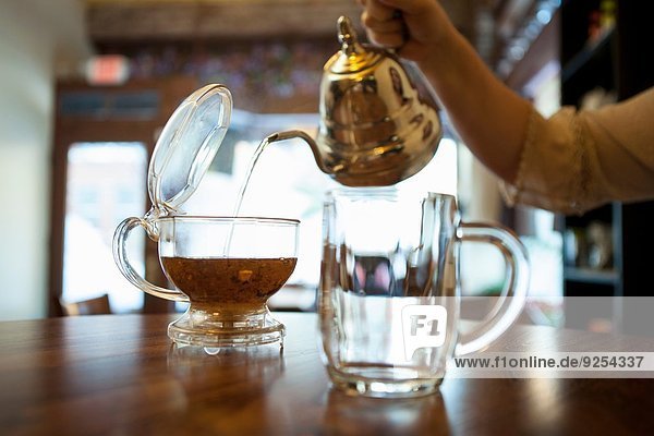 Weibliche Hand gießt Tee auf die Kaffeetheke