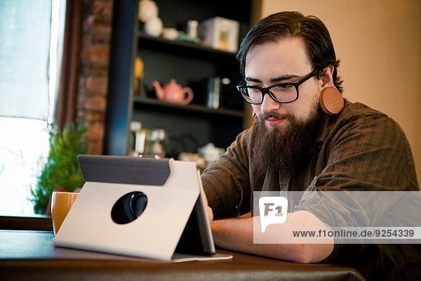 Junger Mann trinkt Kaffee und benutzt digitale Tabletten im Cafe
