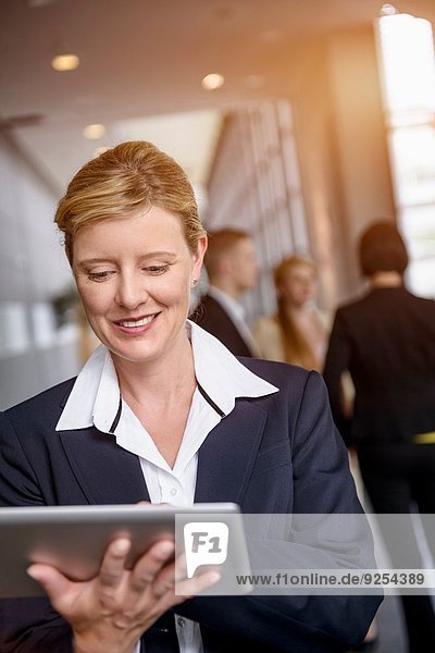 Mature woman using touchscreen on digital tablet in office corridor