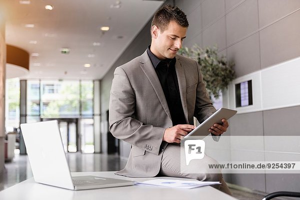 Mid adult businessman on office desk using digital tablet