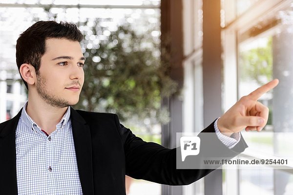 Young businessman pointing out of office window