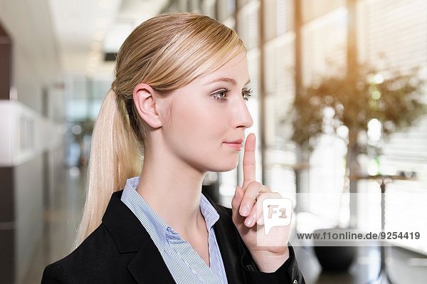 Porträt einer jungen Geschäftsfrau  die den Finger an die Lippen hält.