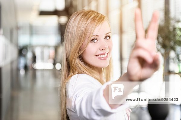 Porträt einer selbstbewussten jungen Geschäftsfrau  die mit der Hand ein Siegeszeichen setzt.