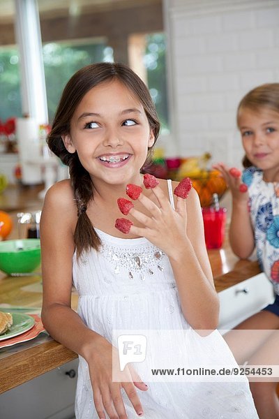 Two mischievous sisters with raspberries on their fingers in kitchen