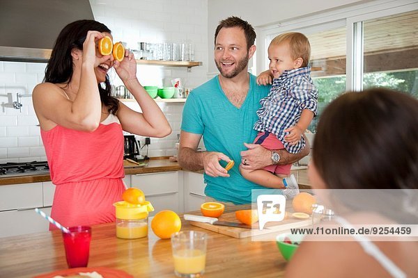 Mutter macht ein Gesicht mit Orangen für ihre Familie an der Frühstückstheke
