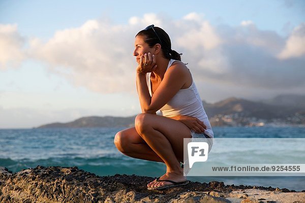 Mid adult woman crouching and gazing at caribbean sea from pier  Spice Island beach resort  Grenada
