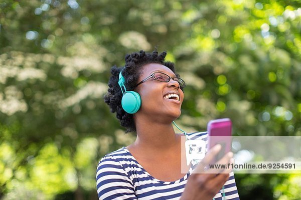 Junge Frau im Park beim Hören und Singen von Musik über Kopfhörer
