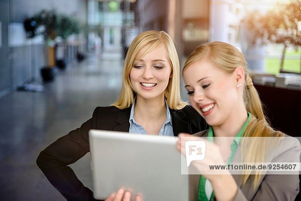 Two young businesswomen looking at digital tablet in office