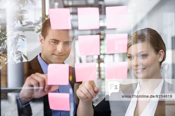 Businessman and woman arranging post it notes on office window