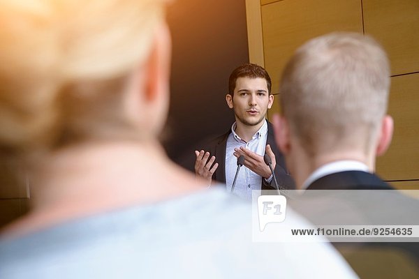 Young businessman speaking to audience in conference room
