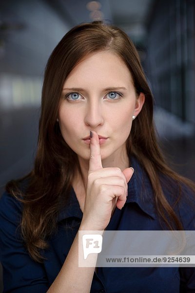 Porträt einer seriösen jungen Geschäftsfrau mit Finger auf den Lippen im Büro