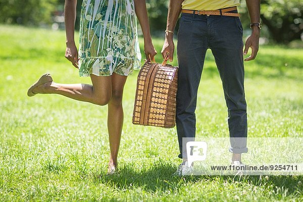 Beschnittenes Bild des jungen Paares mit Picknickkorb im Park
