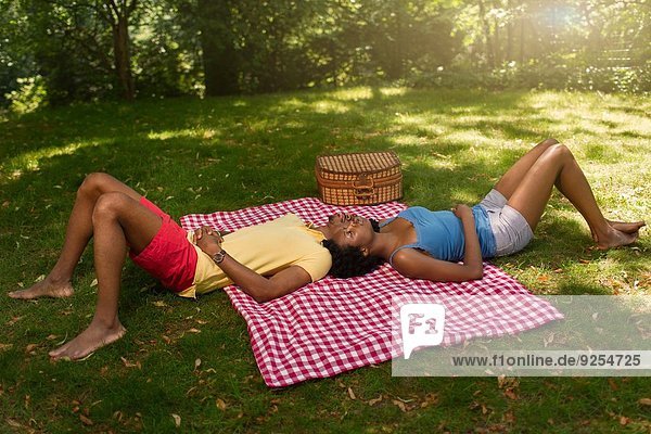 Junges Paar auf Picknickdecke im Park auf gegenüberliegenden Seiten liegend