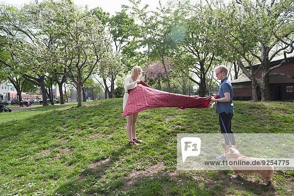 Junges Paar schüttelt Picknickdecke im Park