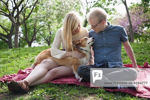 Junges Paar mit Corgi-Hund im Park sitzend