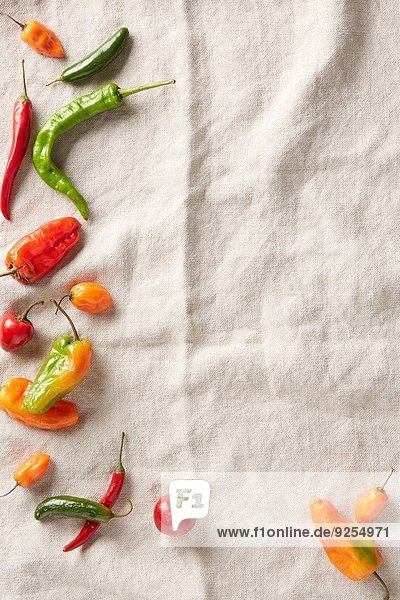 Auswahl von Sommer-Chili-Paprika auf elfenbeinfarbener Leinenoberfläche