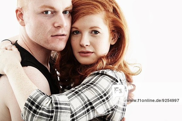 Studio-Porträt eines rothaarigen jungen Paares  das sich von Wange zu Wange umarmt.