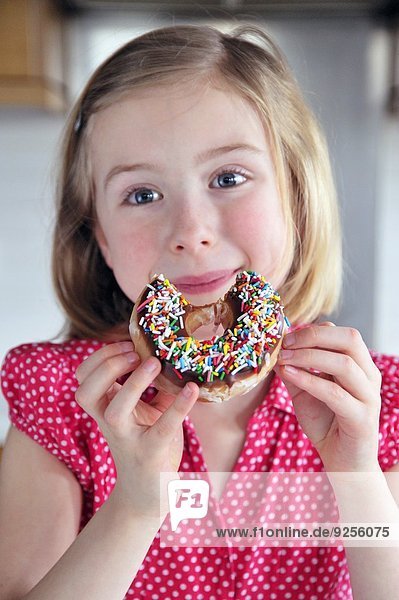 Kleines Mädchen isst Doughnut mit Zuckerstreuseln