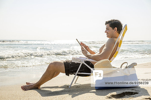 Side view of man sitting on deckchair and using digital tablet