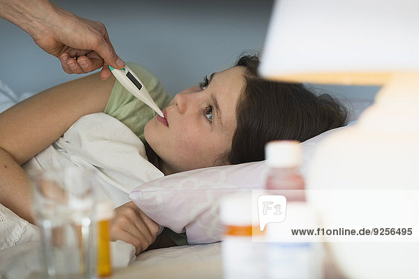Sick girl (8-9) with thermometer in mouth