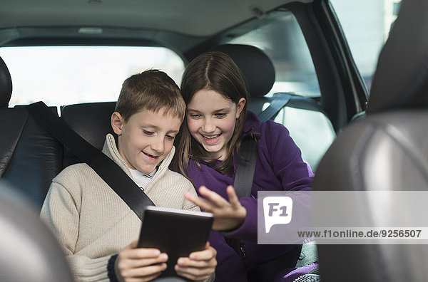 Boy and girl (8-9  10-11) using digital tablet in car