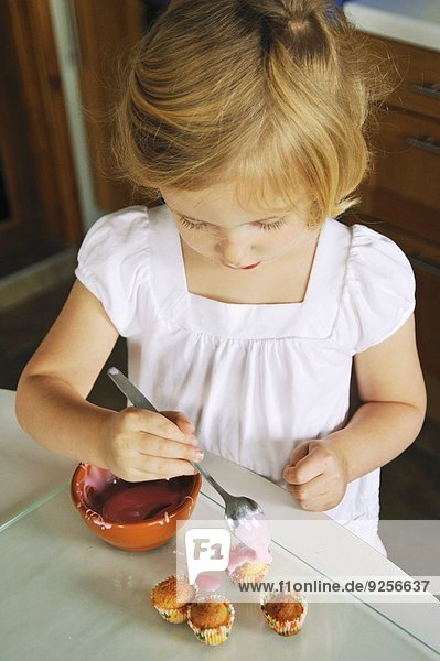 Kleines Mädchen verziert Minimuffins in der Küche