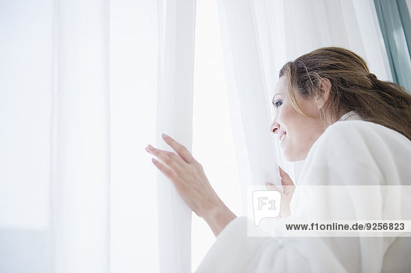 Woman wearing bathrobe looking through window