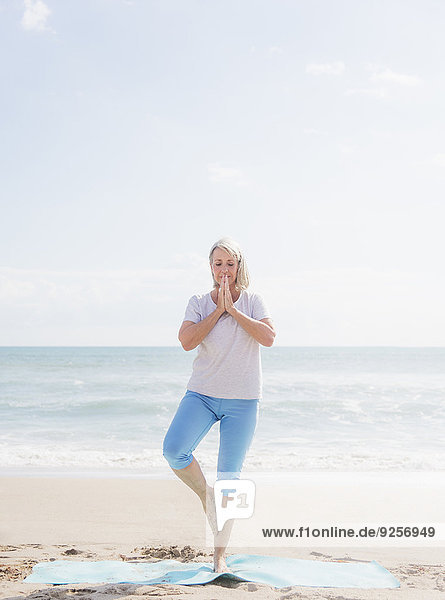 Senior woman practicing yoga on beach
