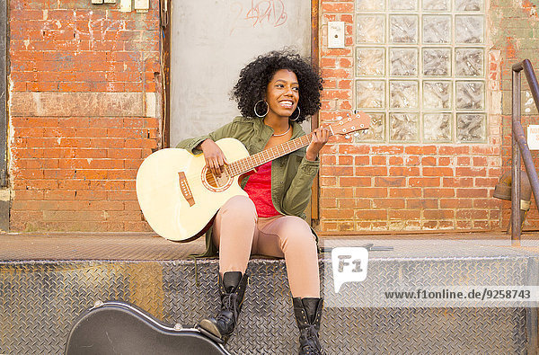 Mixed race woman playing guitar in city