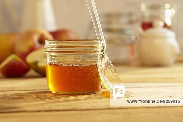 Ein Glas Honig mit Löffel vor frischen Äpfeln