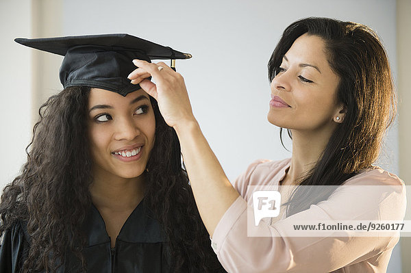 Mother adjusting teenage daughter's graduation cap