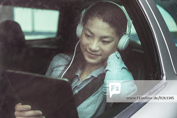 Mixed race teenage girl using digital tablet in backseat of car