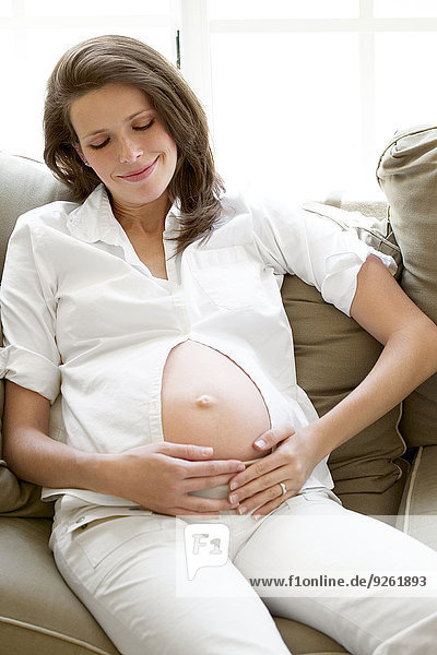 Pregnant woman holding her belly on sofa