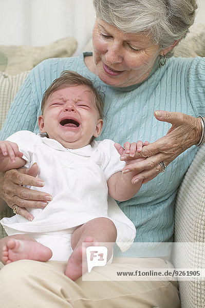 Senior woman with crying granddaughter on sofa