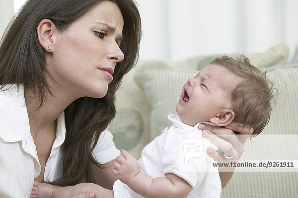 Mother comforting crying baby on sofa