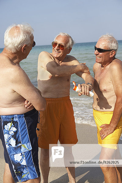 Senior Senioren eincremen verteilen Mann Strand Sonnencreme auftragen
