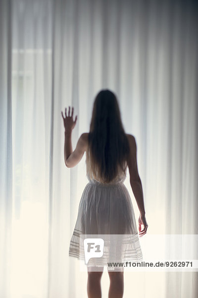Mystische junge Frau steht vor einem weißen Vorhang  Rückansicht