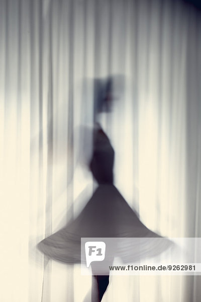 Silhouette einer jungen Frau  die vor einem weißen Vorhang tanzt.