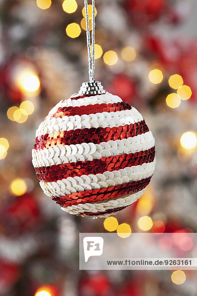 Weihnachtskugel geschmückt mit roten und weißen Pailletten vor verschwommenen Fackeln