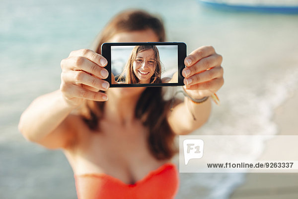 Indonesien  Gili Inseln  Frau am Strand zeigt Smartphone mit ihrem Selfie