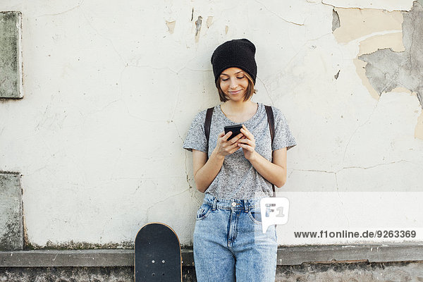 Porträt einer lächelnden jungen Skateboarderin mit Smartphone